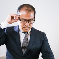 眼鏡を調整しながら俯くスーツ姿の男性会社員の写真