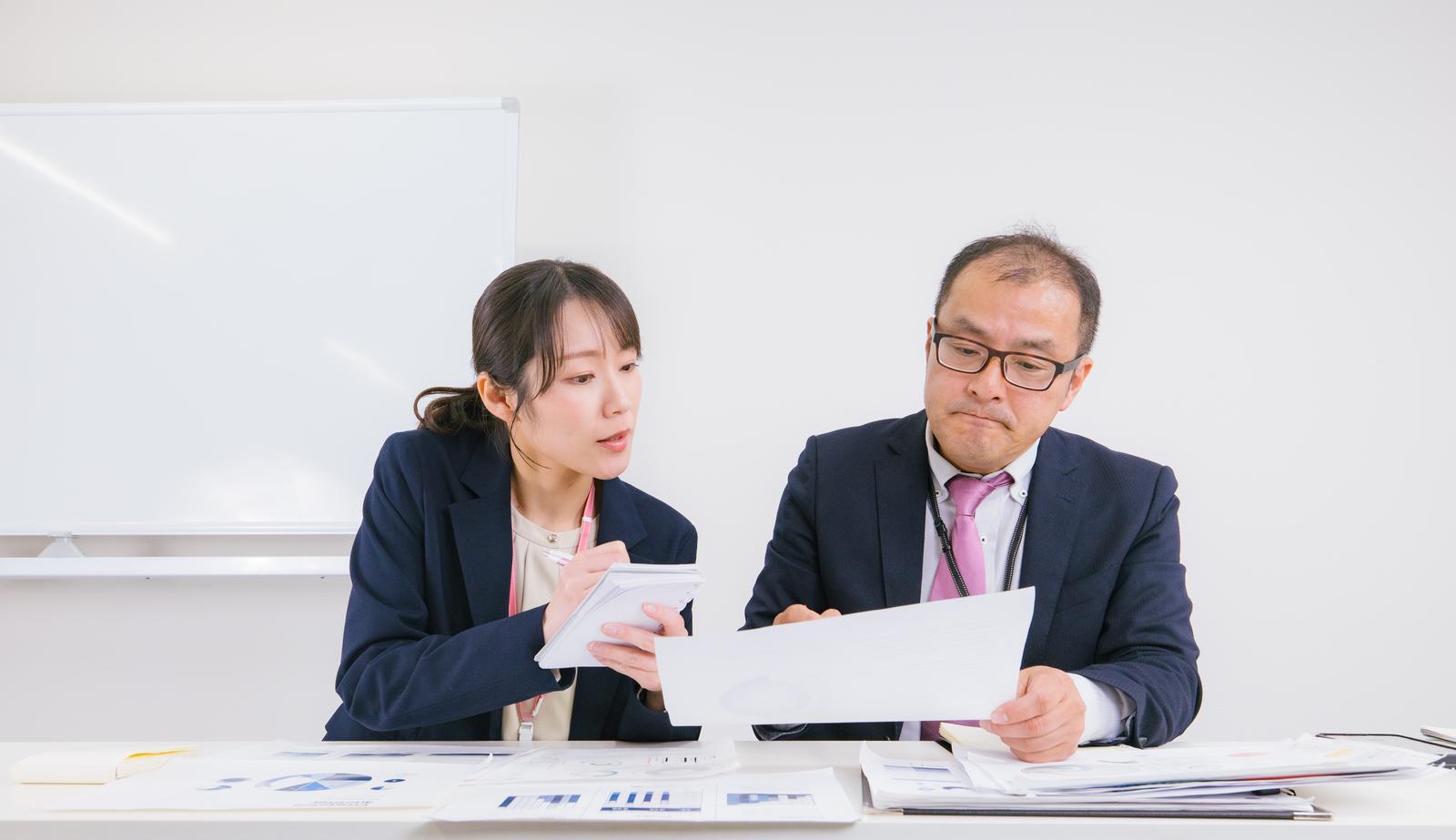 資料を確認しながら打ち合わせをする男女の会社員［モデル：高木桂一 SAKI］