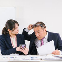 「ちょっと待ってよ」と驚いて書類を確認する会社員の写真