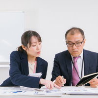 会議室で書類を確認しながら意見交換する男女の会社員の写真
