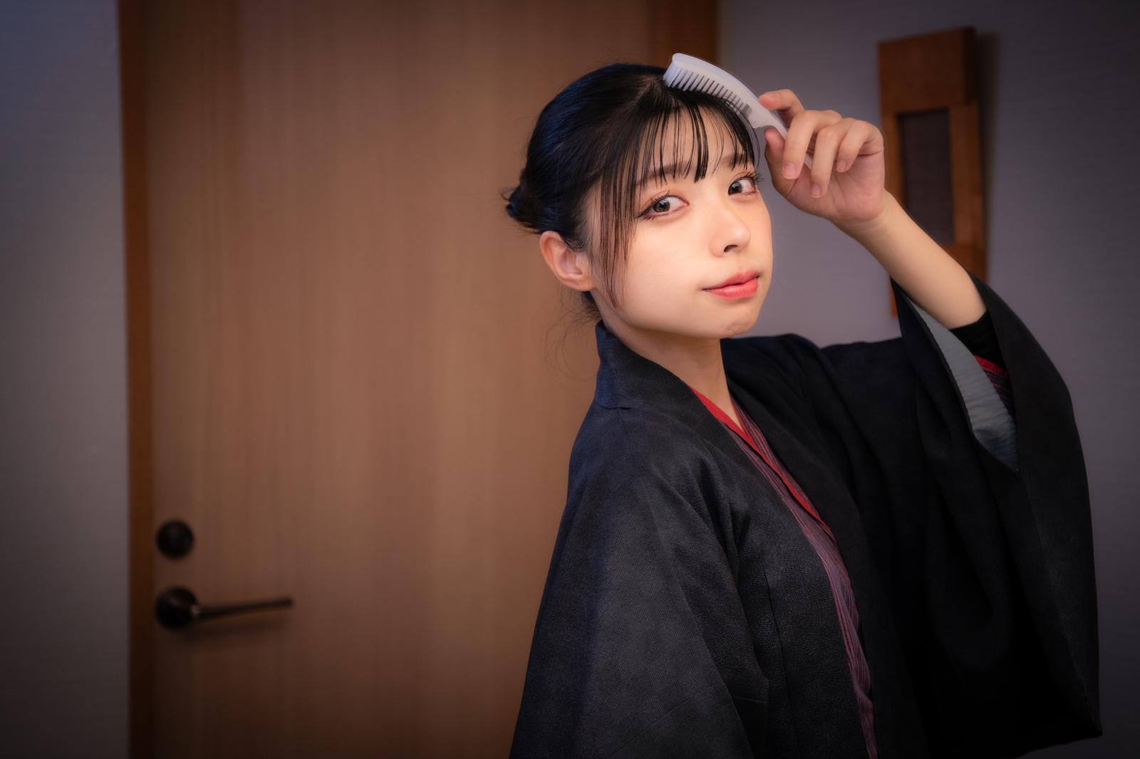 クシで髪をセットする女性が横向きで微笑んでいる［モデル：高尾実生］