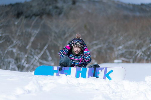 雪山のゲレンデで転倒するスノーボード初心者の女性