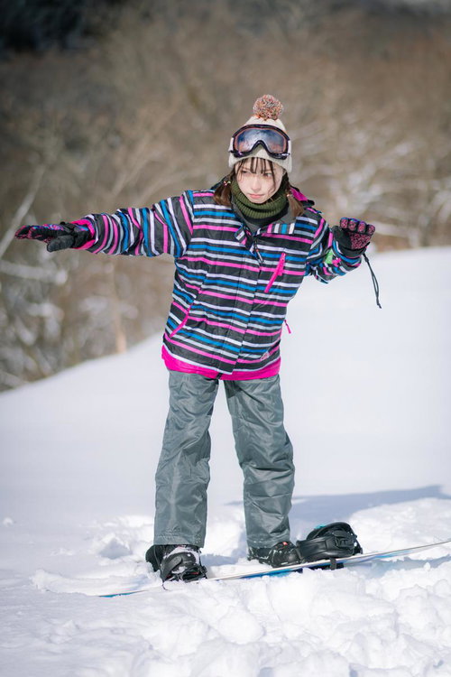 バランスを取りながらゲレンデでスノーボードを滑る女性