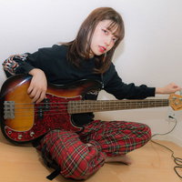 チェック柄パジャマ姿でベースをチューニング中の女性ミュージシャンの写真