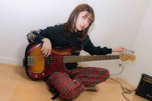 チェック柄パジャマ姿でベースをチューニング中の女性ミュージシャン