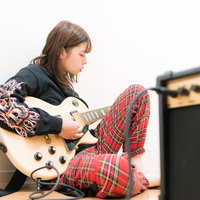 ギターを持ってアンプの前に座る女性ギタリストの写真