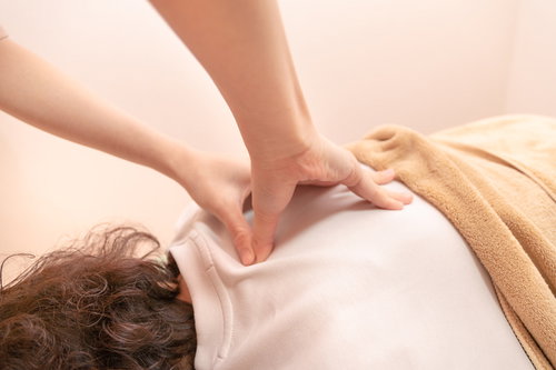 肩の筋肉を押すマッサージ施術、セラピストによる指圧とリラックス効果