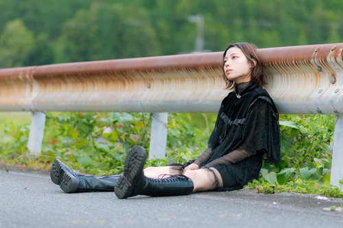 ガードレールに寄りかかって座り込むポーズの女性