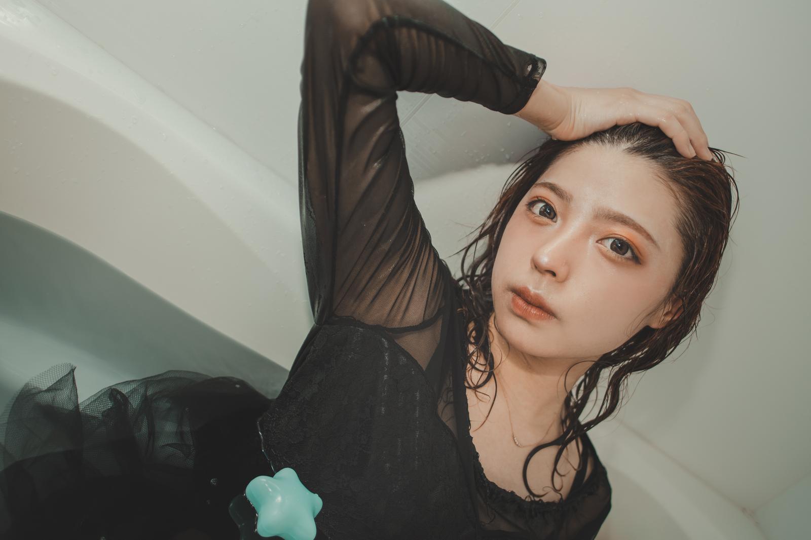 黒いシャツを着た女性が髪をかきあげてリラックスした表情で上向きでいる［モデル：高尾実生］