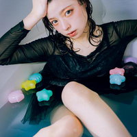 浴槽の中でカラフルなバスボムに囲まれながら頭に手を当てる女性の写真