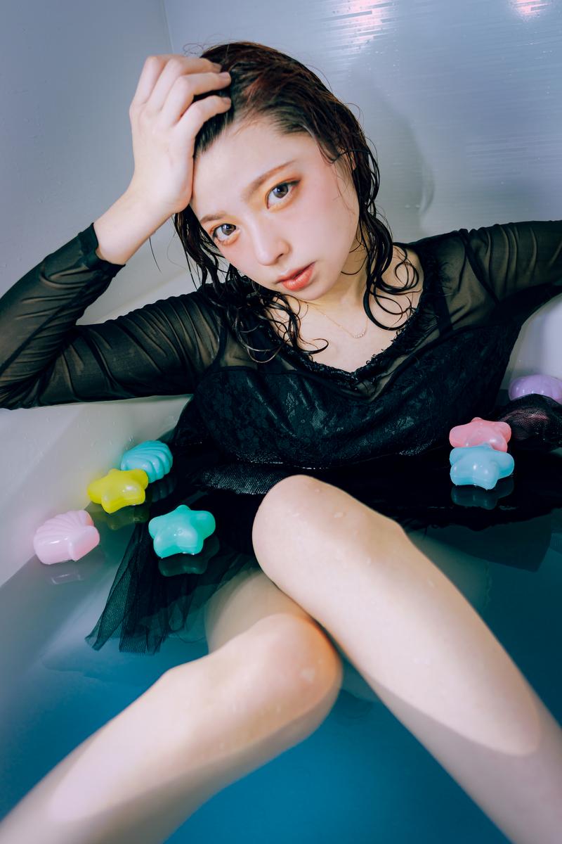 浴槽でカラフルなバスボムに囲まれて頭に手を当てる女性