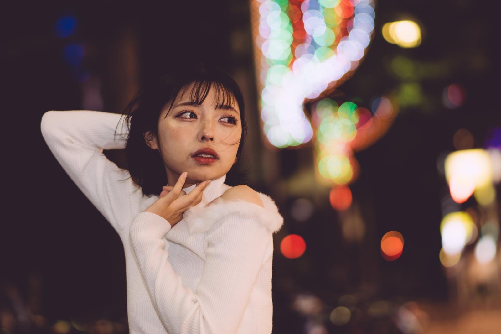 白いトップスを着た女性が夜の街中でネオンライトに包まれている［モデル：高尾実生］