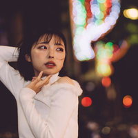 ぼやけた街灯やネオンに包まれる夜の繁華街の女性の写真