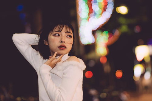 ぼやけた街灯やネオンに包まれる夜の繁華街の女性