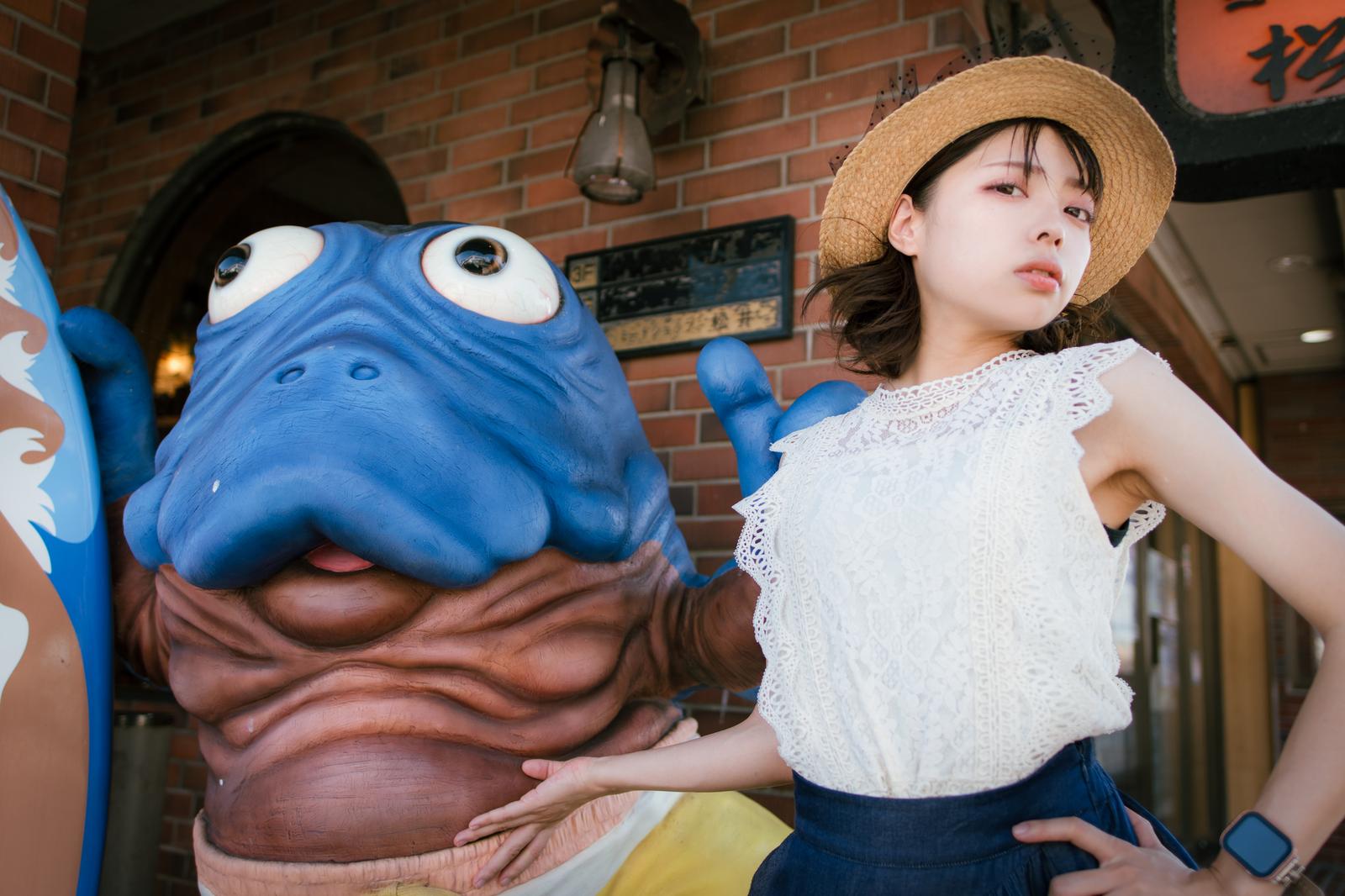 海坊主のオブジェの横に座る麦わら帽子姿の女性［モデル：高尾実生］