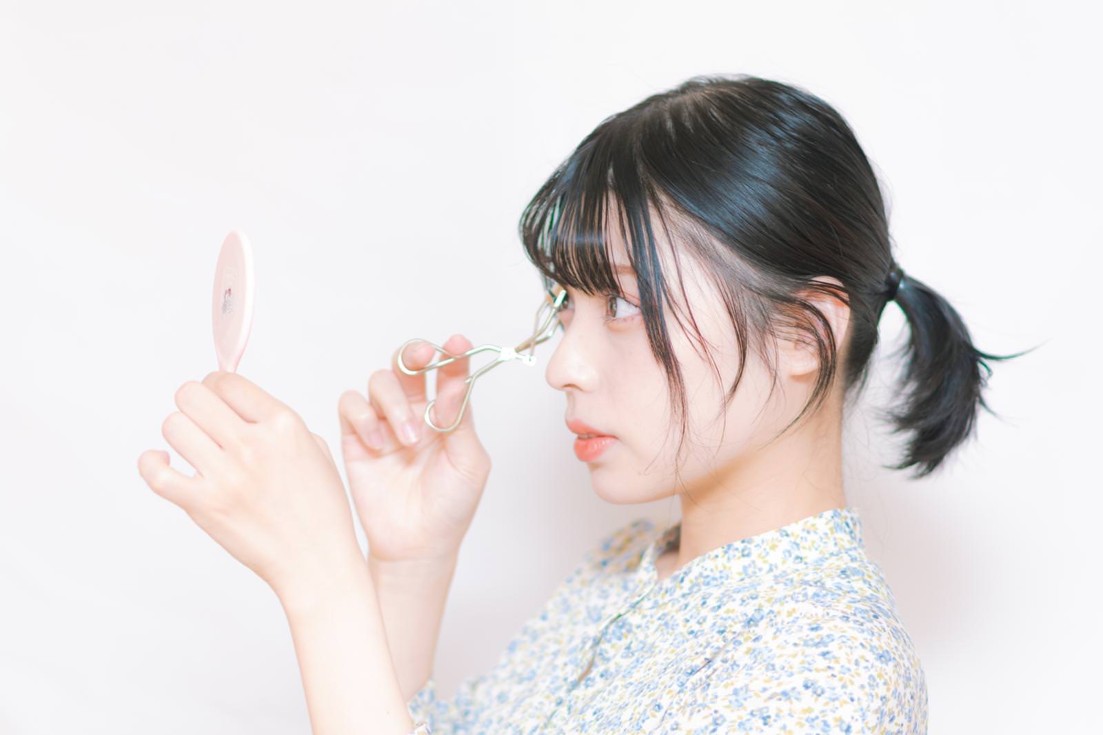 ビューラーでまつ毛をカールさせている女性の横顔［モデル：高尾実生］