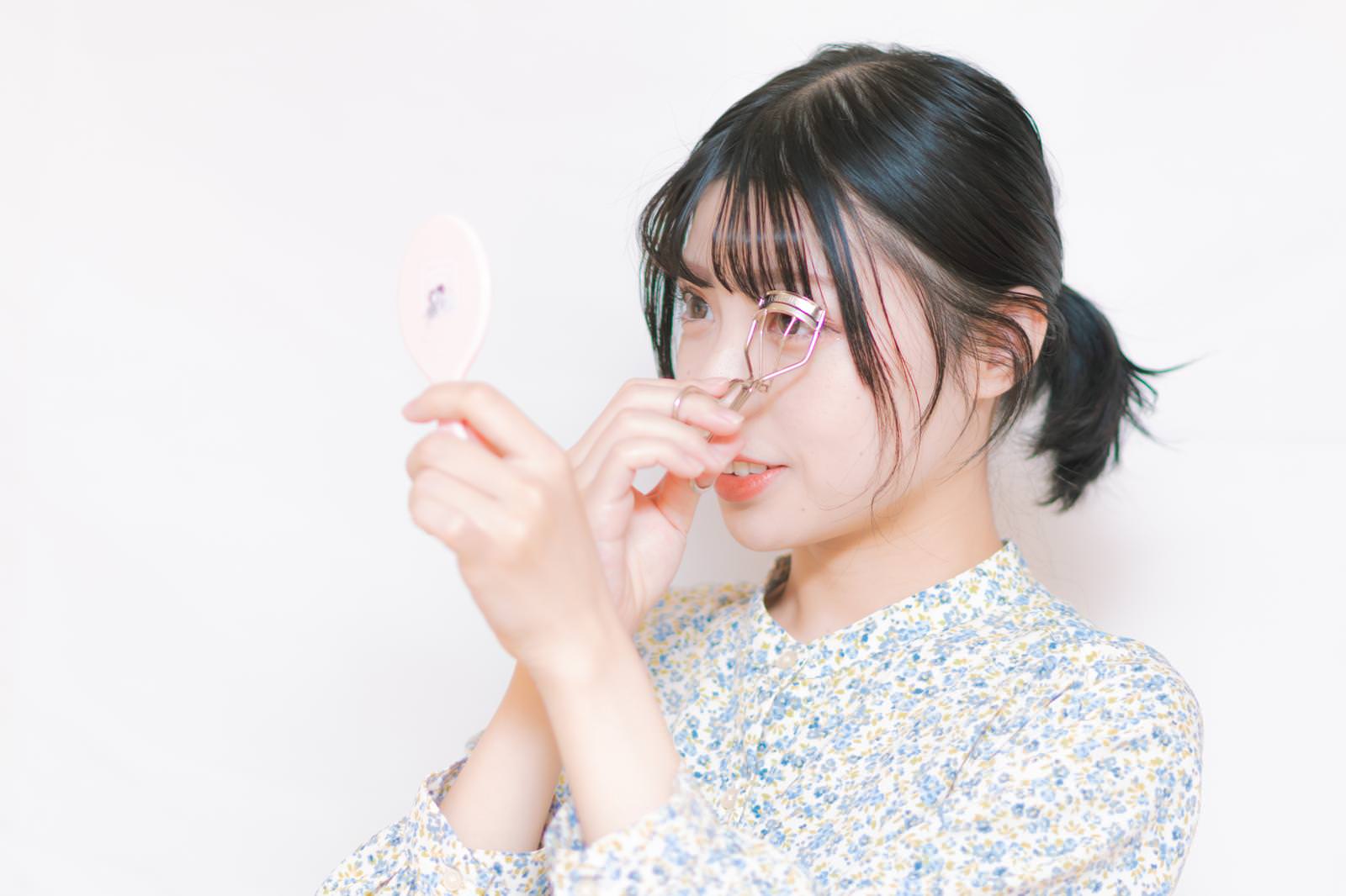 ビューラーを使ってメイクする眼鏡をかけた女性の横顔［モデル：高尾実生］