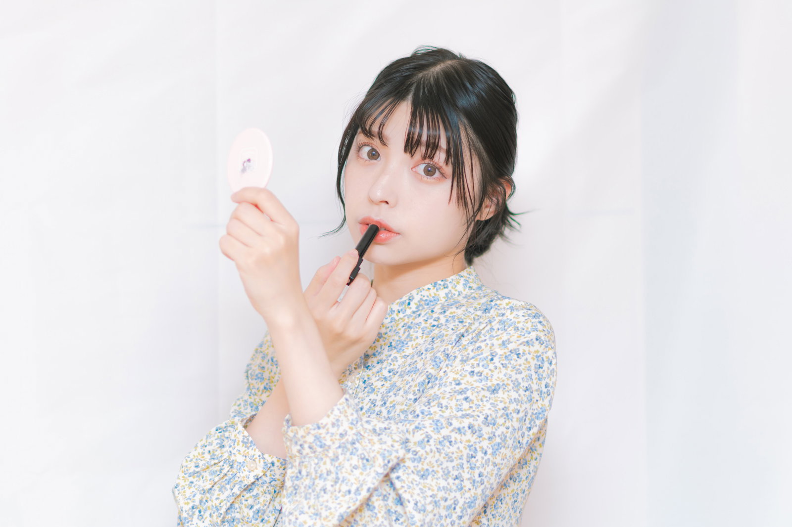 手鏡を持ちながら口紅を塗る女性［モデル：高尾実生］