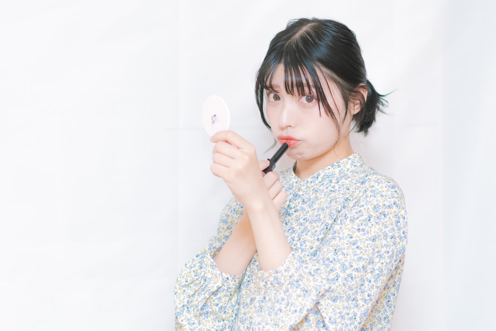 口紅を手に持ち、赤いリップメイクを見つめる女性［モデル：高尾実生］