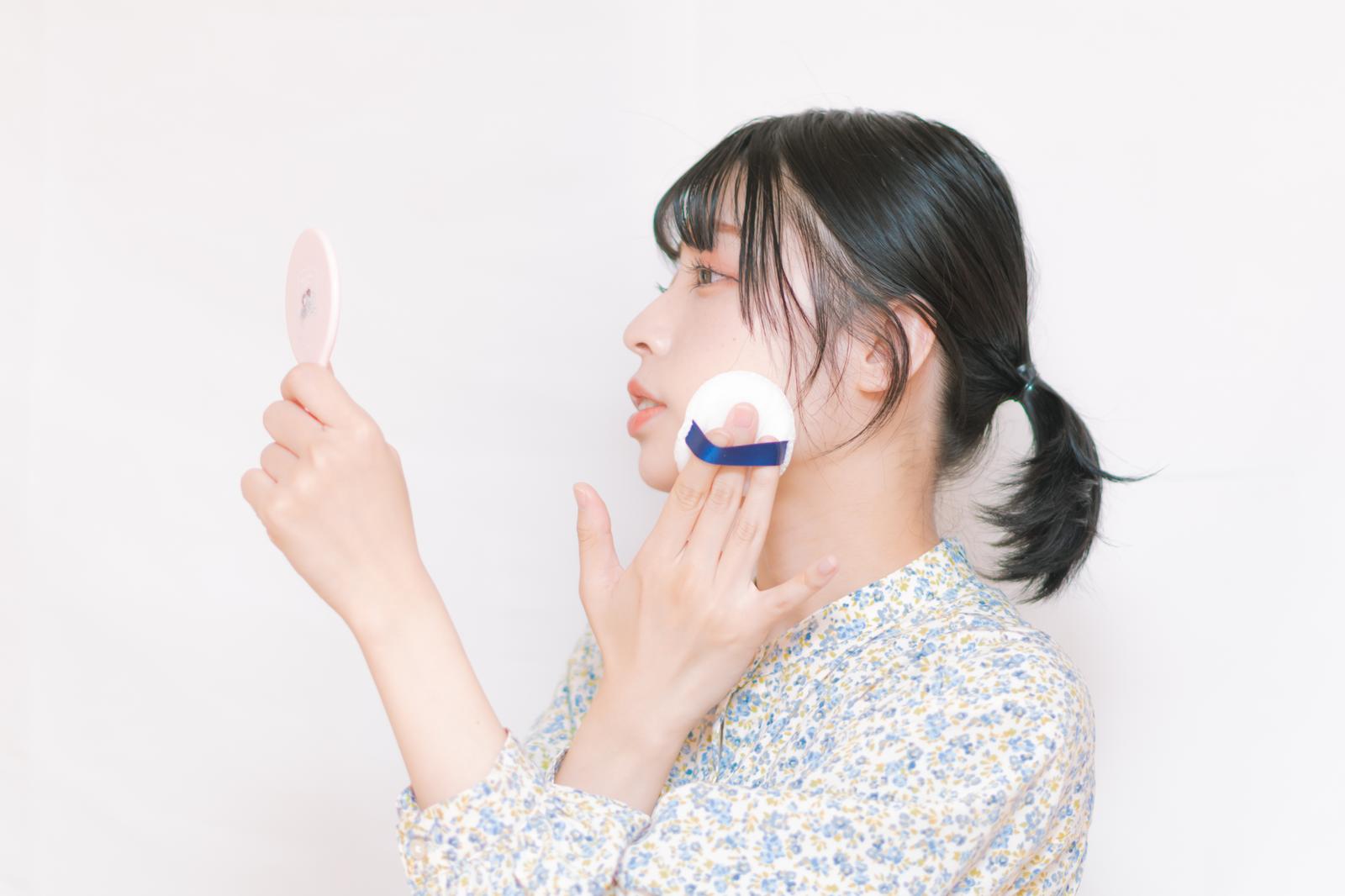 パフで頬にコンプレクションを仕込む女性の横顔と鏡［モデル：高尾実生］