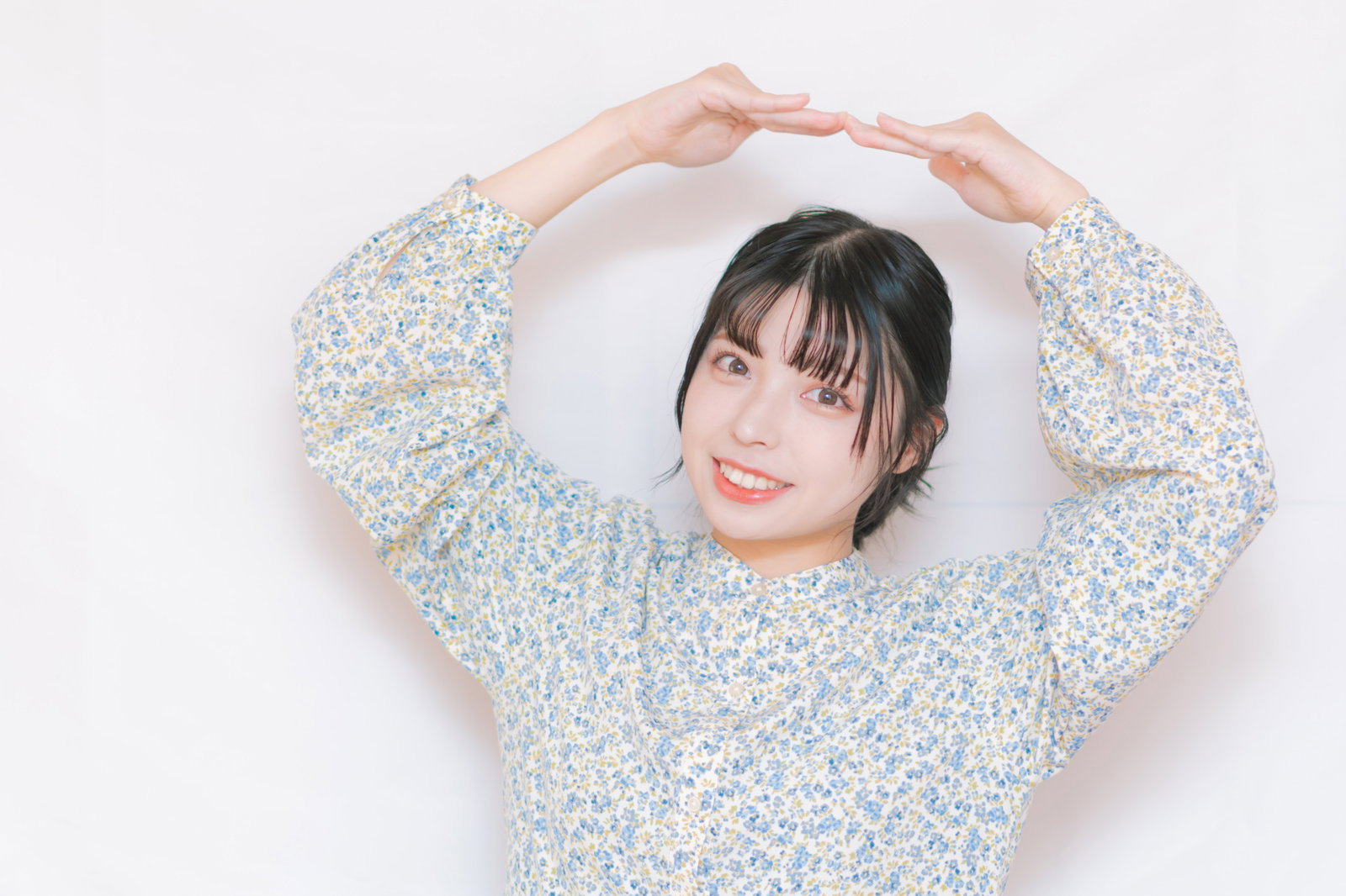 両手でハート型を作って笑顔で見上げる女性［モデル：高尾実生］