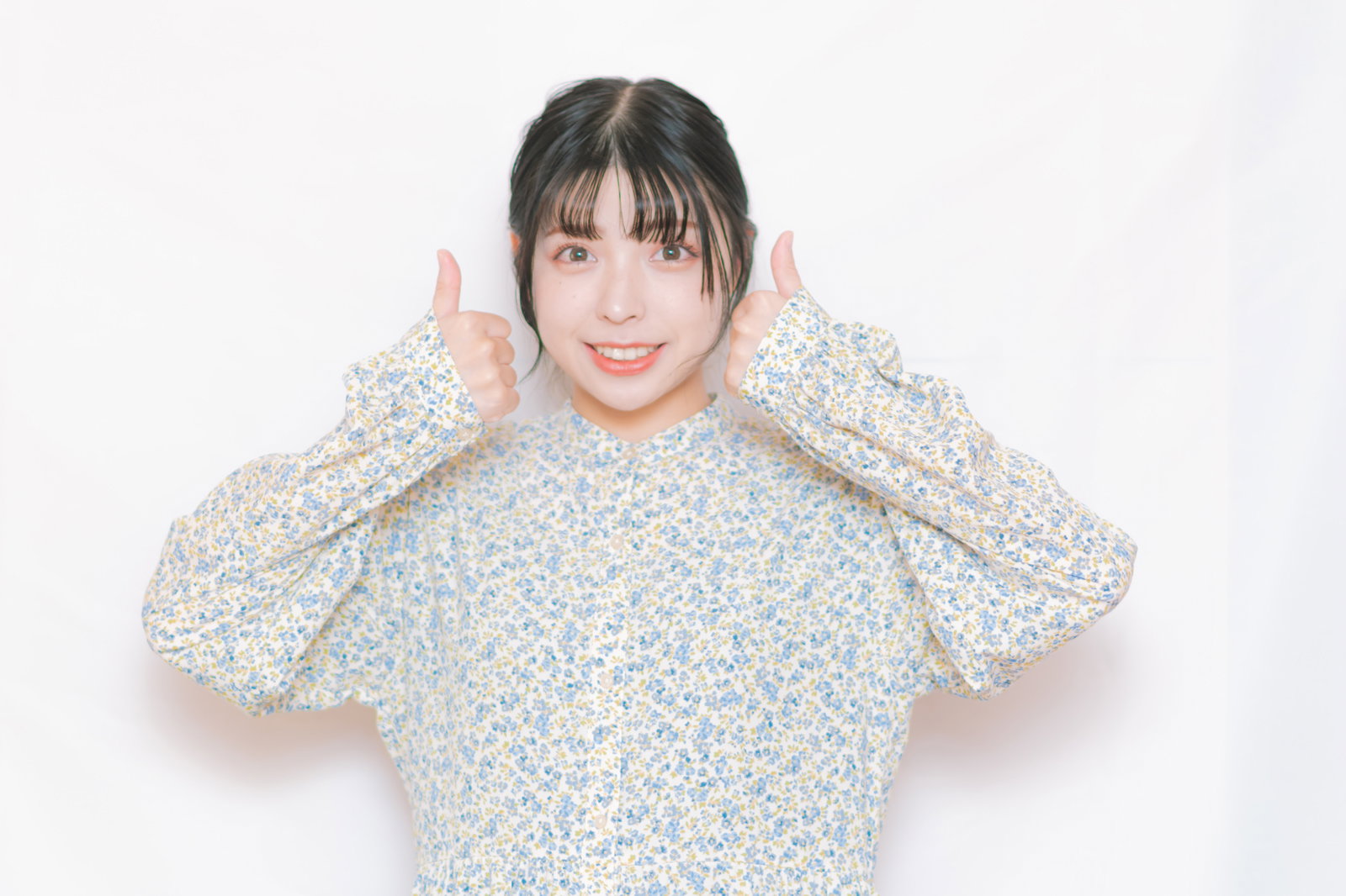 両手で親指を立ててOKポーズをする笑顔の女性、花柄シャツ着用［モデル：高尾実生］