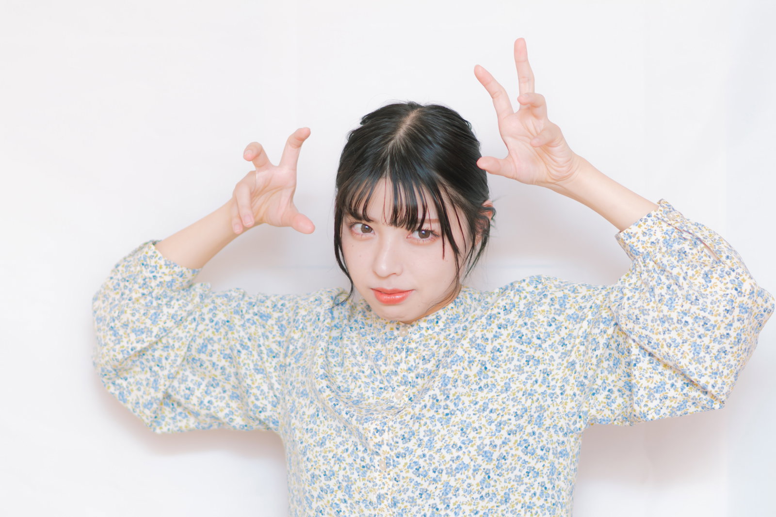 両手を上げてファイティングポーズをとる女性、白とブルーの花柄シャツ姿［モデル：高尾実生］
