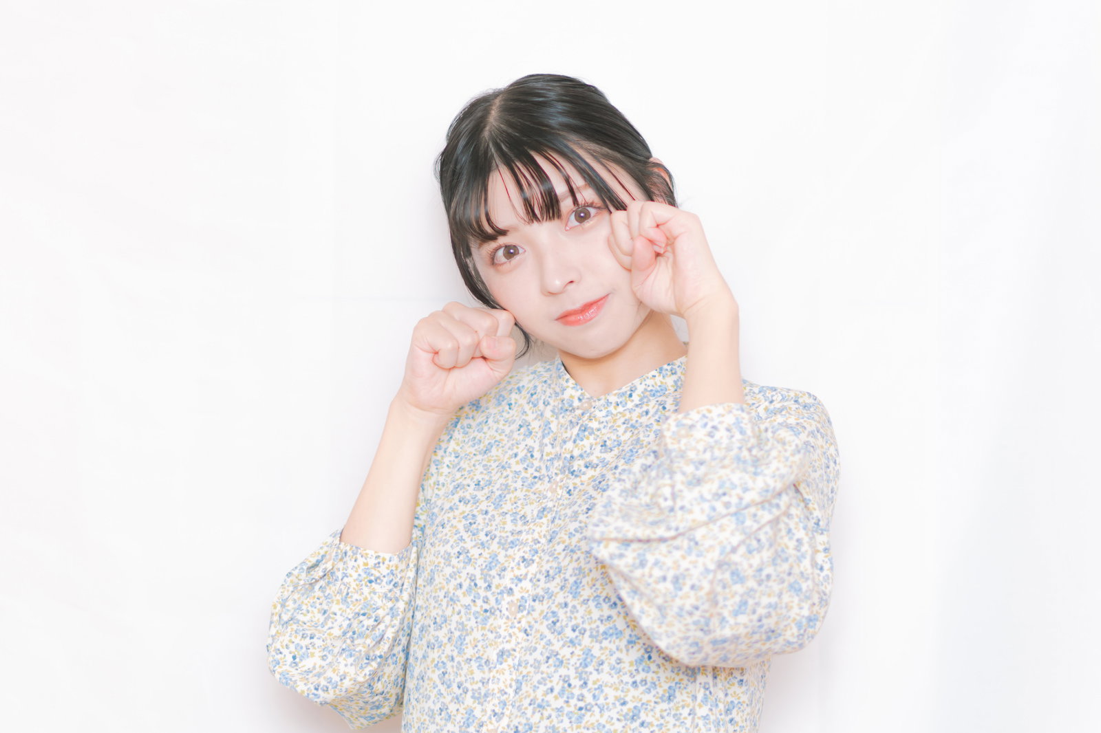 にゃんにゃんポーズをして笑う花柄ブラウスの女性［モデル：高尾実生］