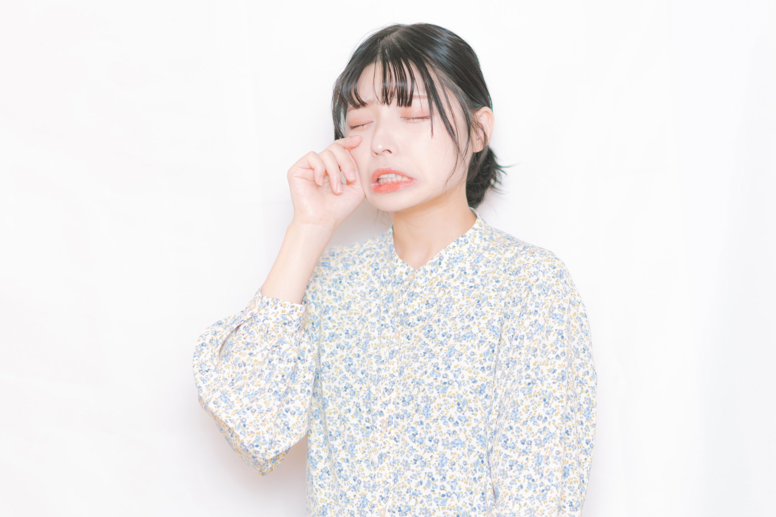 涙をこぼして目を閉じる女性が右手で顔に触れている［モデル：高尾実生］