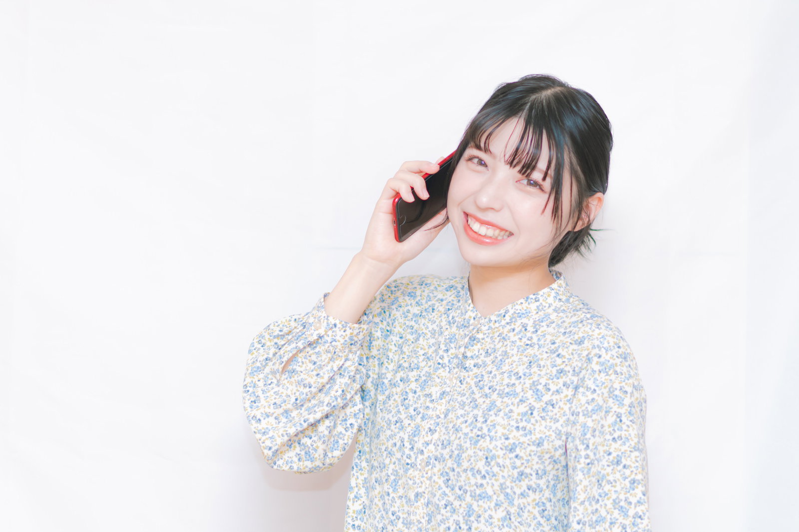 電話で笑顔になる若い女性［モデル：高尾実生］