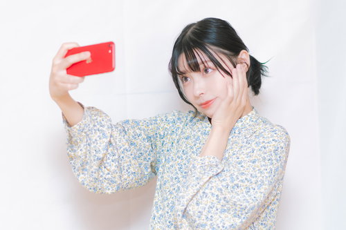 赤いスマートフォンで自撮りする女性の歯痛表情