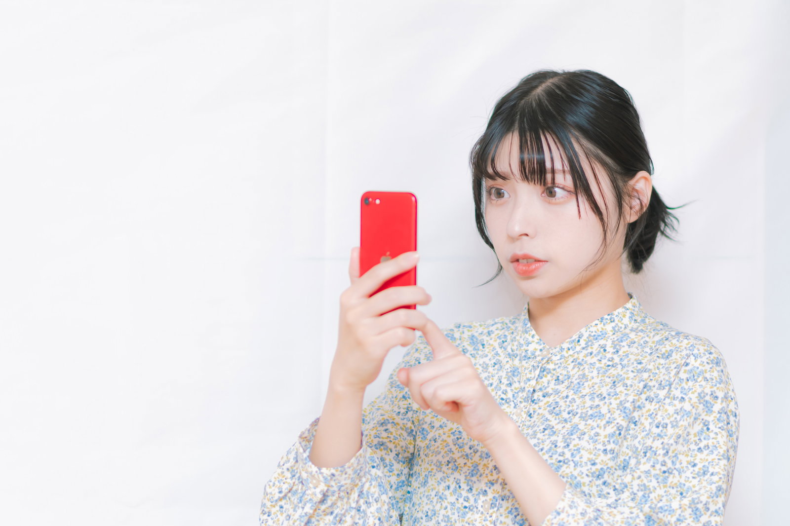 スマホを見て驚く花柄ブラウスの女性［モデル：高尾実生］