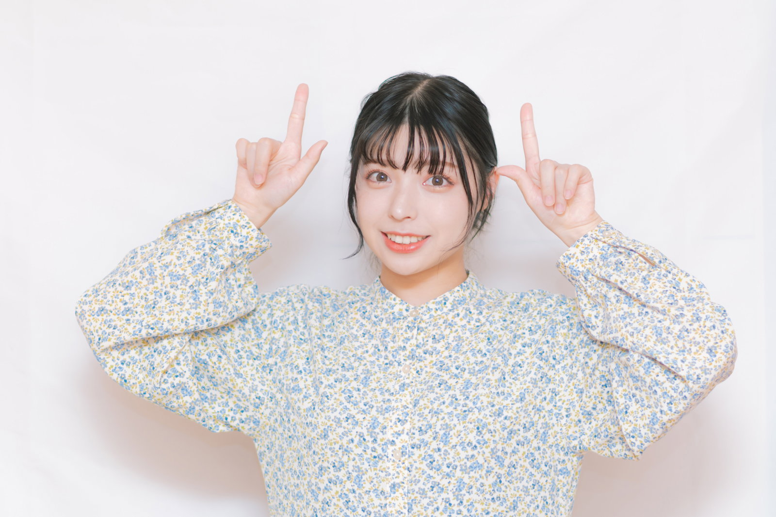 両手でピースサインをして笑う花柄シャツの女性［モデル：高尾実生］