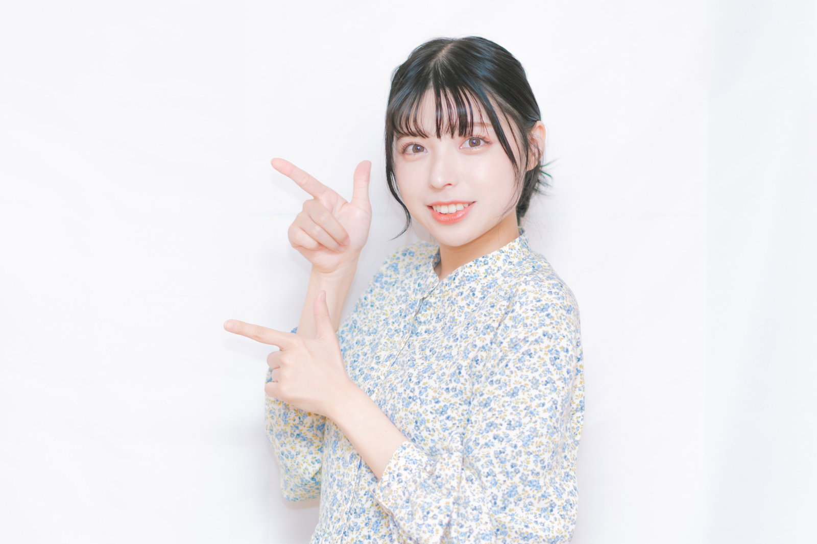 左側を両手の指で指さして笑う女性［モデル：高尾実生］