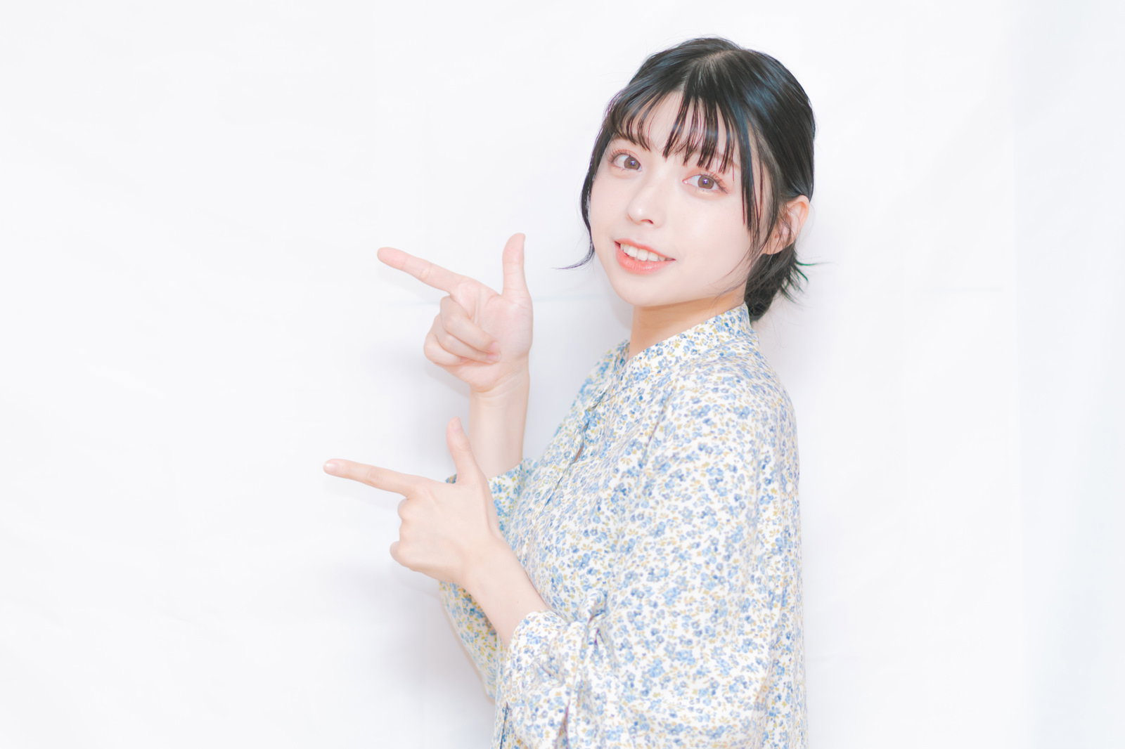 両手で指を差す笑顔の女性がジェスチャーで指示をしている［モデル：高尾実生］