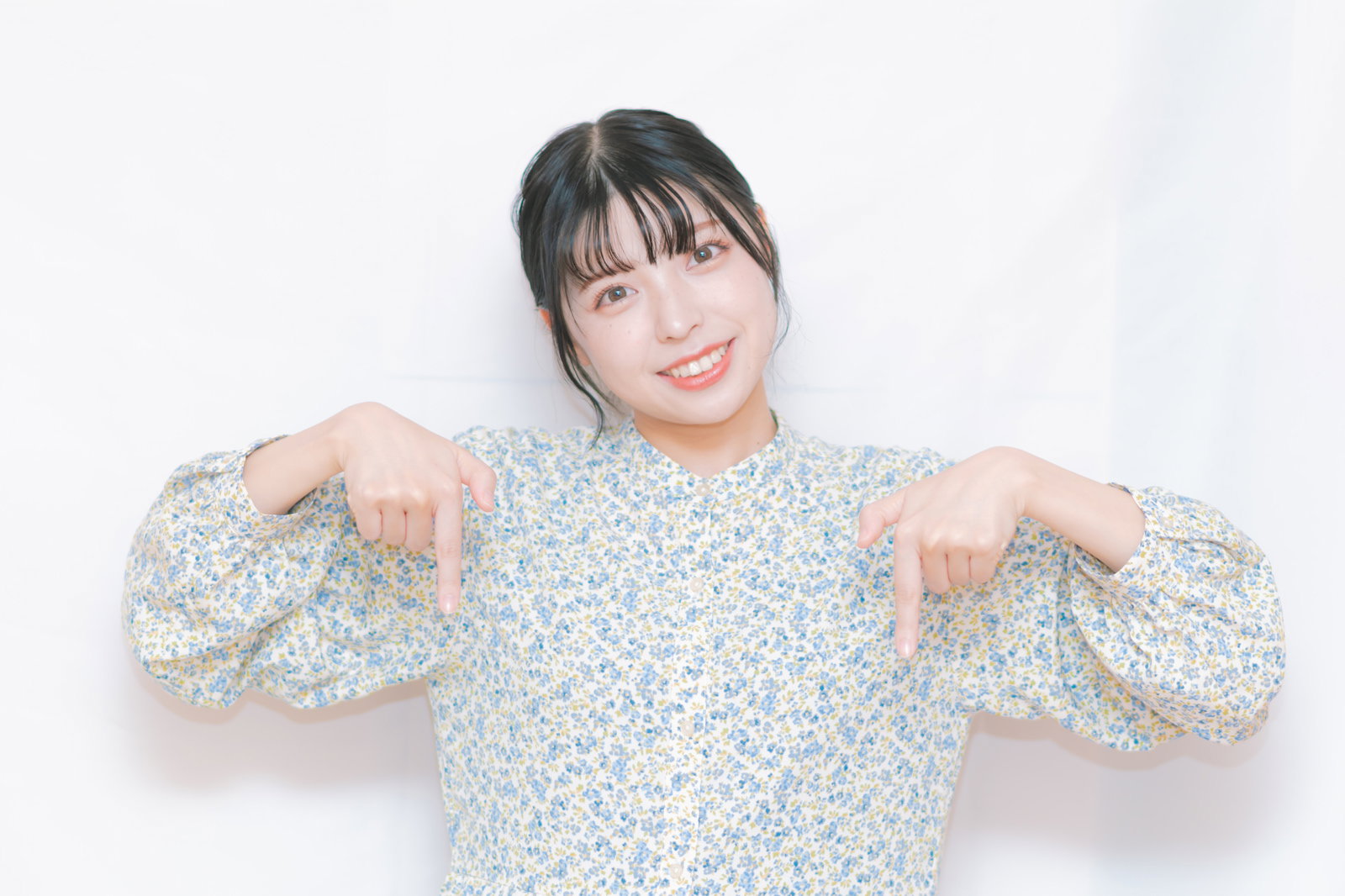 花柄トップスの女性が両手で下を指して笑顔でポイント［モデル：高尾実生］