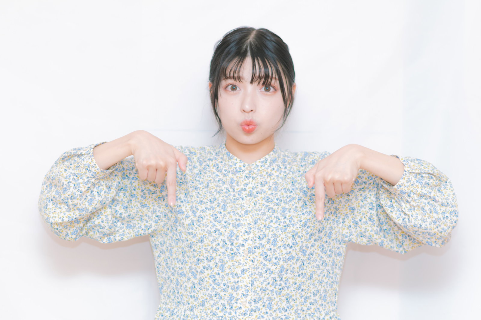 両手を横に広げて下を指さし、驚いた表情で口を開ける黒髪の女性［モデル：高尾実生］