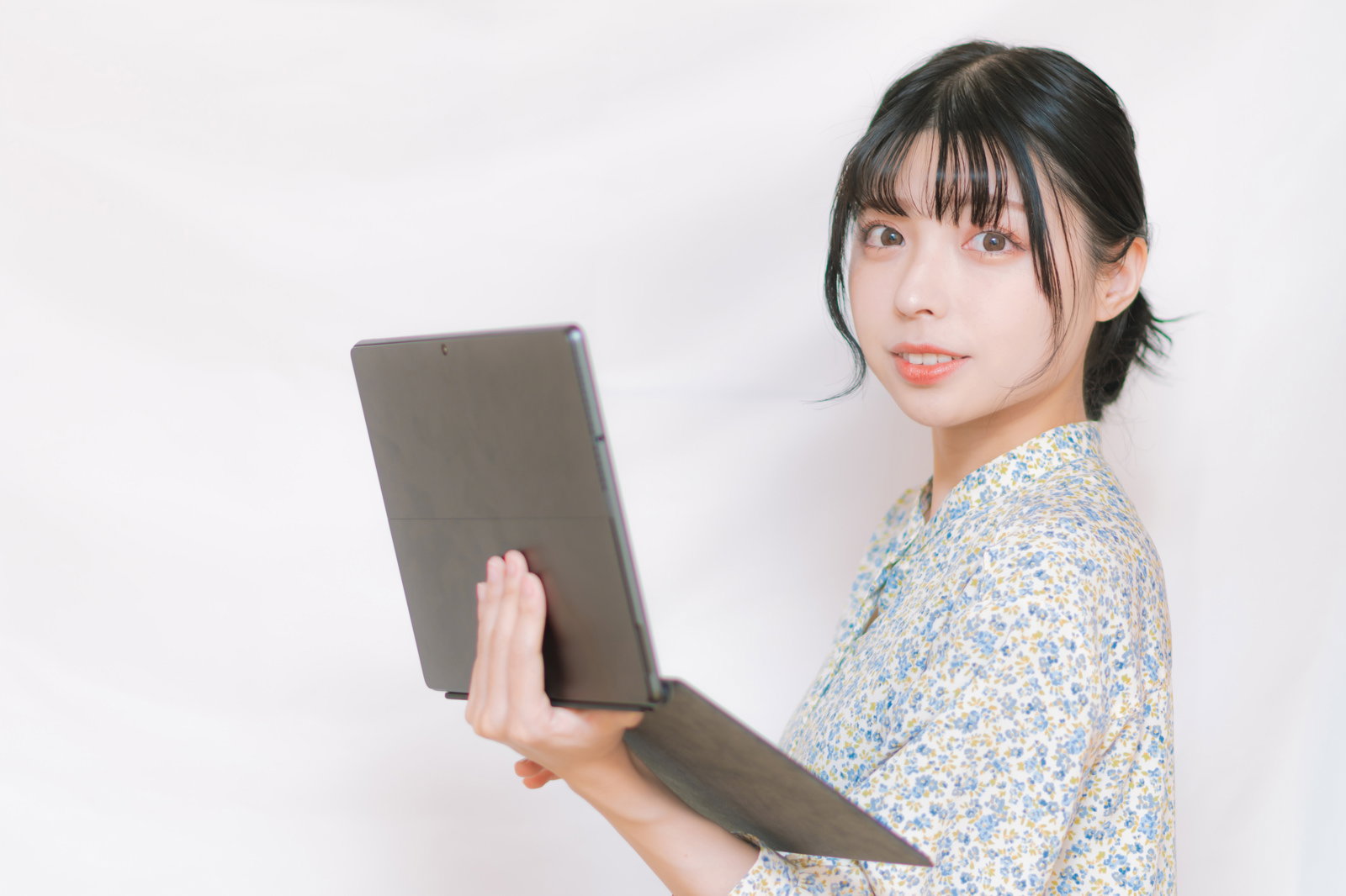 タブレット端末を片手に持って振り返る黒髪ショートの女性［モデル：高尾実生］