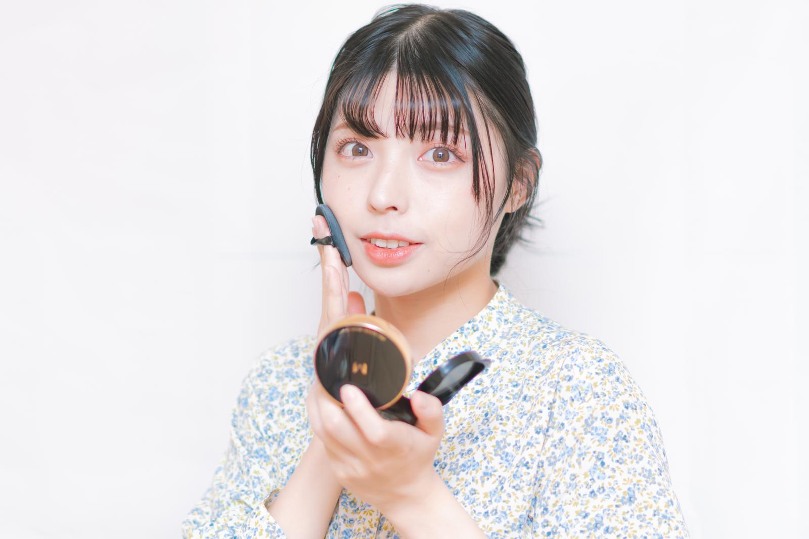 ヘッドフォンを付けてコスメのパフを持つ女性が笑顔で見つめている［モデル：高尾実生］