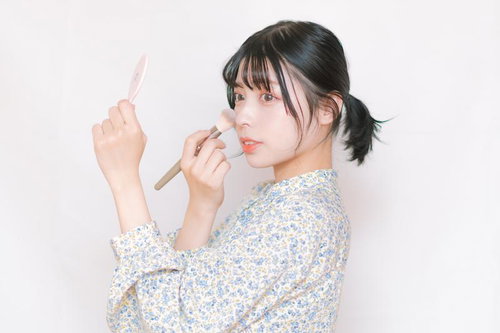 チークブラシでメイクアップを仕上げる女性の横顔