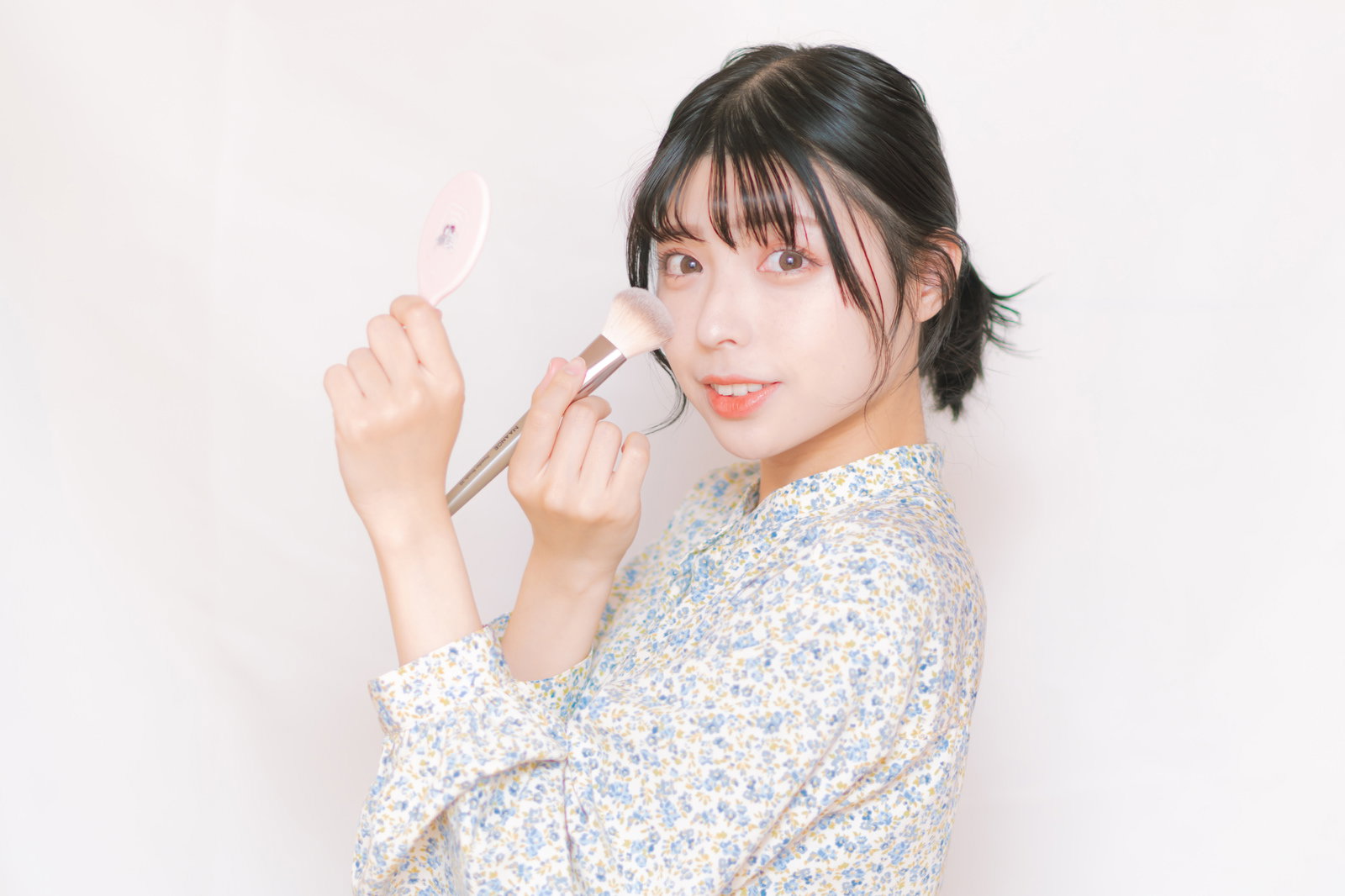 チークブラシを頬に当ててメイクする女性［モデル：高尾実生］