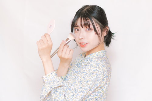 チークブラシを頬に当てる女性のメイクアップ