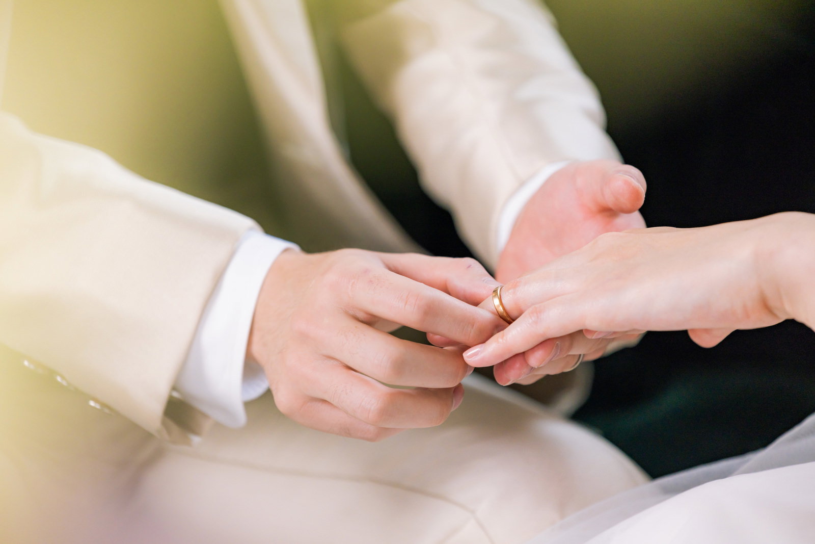 白いウェディングドレスの新婦の左手薬指に結婚指輪をはめる男性の手［モデル：たけべともこ］