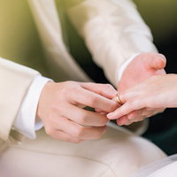 白いウェディングドレスの花嫁の左手薬指に結婚指輪をはめる瞬間の写真