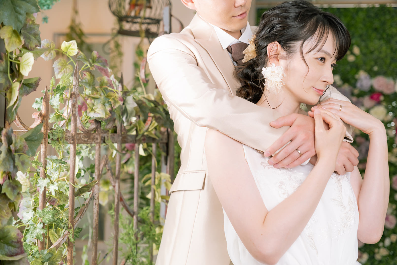 緑のガーデンでウェディングドレスの新婦を優しく抱きしめる新郎［モデル：たけべともこ］