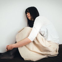 買ったばかりのベッドが小さくて憂鬱な高身長ガール、白シャツで体育座りの写真