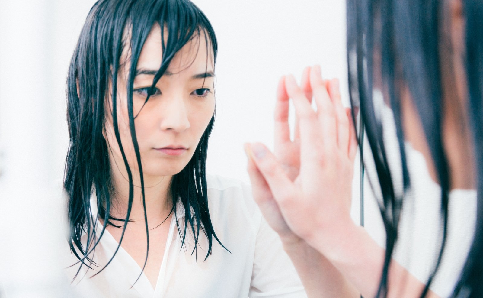 白シャツの黒髪女性が鏡に手をついて下を向く［モデル：たけべともこ］