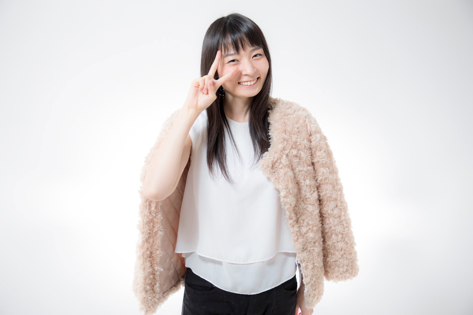 ベージュのアウターを着た女性が笑顔でピースサインをしている［モデル：たけべともこ］