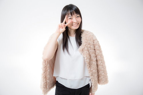 笑顔でピースサインする白トップスの女性のポートレート