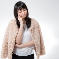 ベージュのファーを羽織り考え込む女性の写真